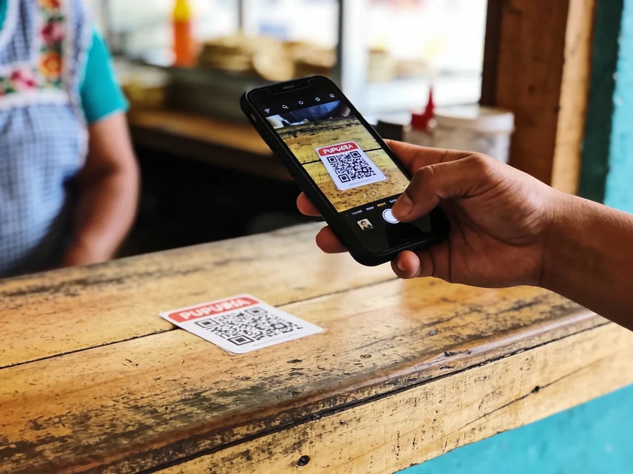 Clienta escaneando con su celular el código QR pegado en el mostrador de la pupusería